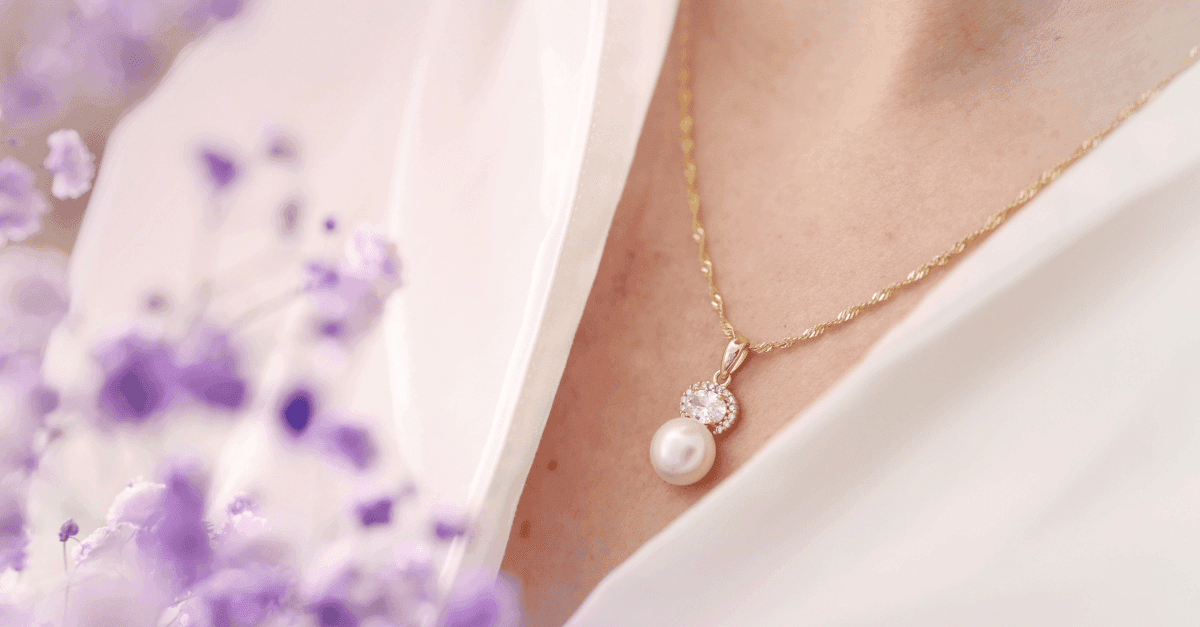 Nærbilde av en kvinne med halssmykke og perleanheng. Kvinnen har hvit bluse og holde lille blomster