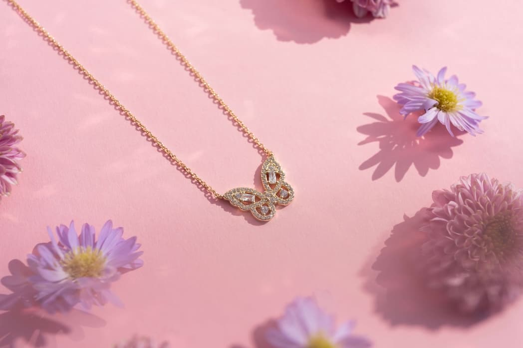 Gullsommerfuglkjede som glitrer på rosa bakgrunn med spredte lilla blomster rundt.