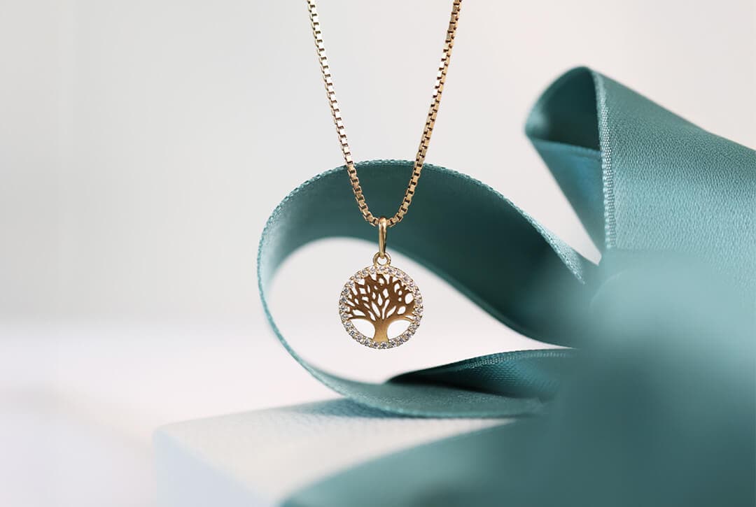 Gullfarget livets tre-anheng på en delikat kjede, hengende foran et blågrønt bånd, og skaper en elegant og fredfull komposisjon.