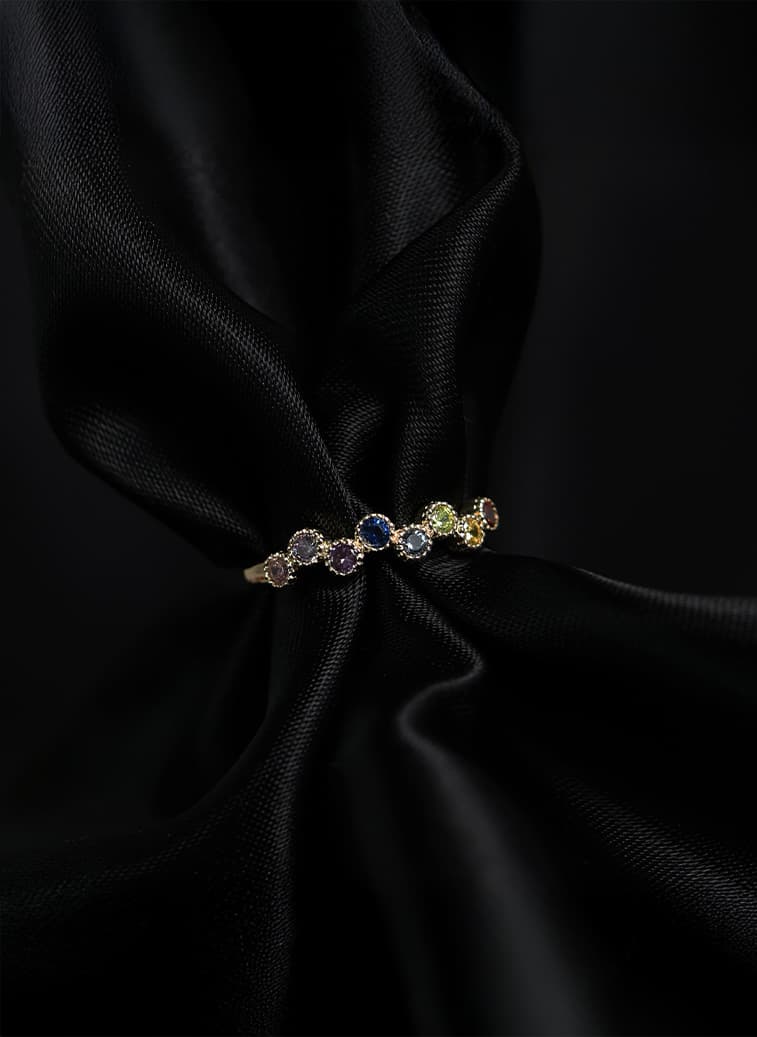 En gullring med en rekke fargerike edelstener, presentert på et elegant, svart satengstoff.